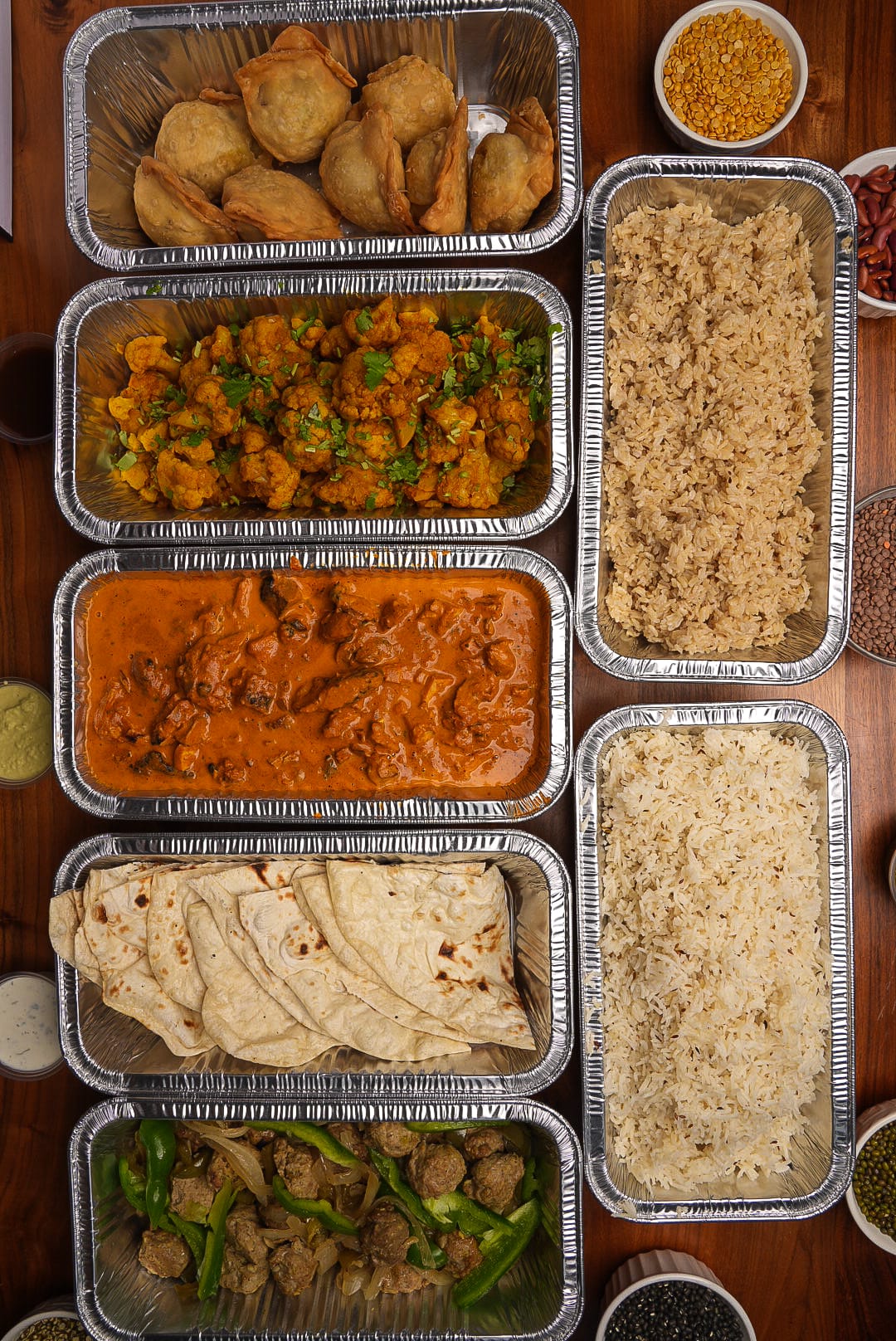 Overhead view of a full NaanStop catering spread with kofta, roti, chicken tikka masala, aloo gobi, samosas and rice